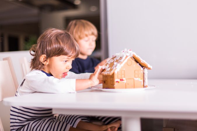 Two children sitting on chair making gingerbread house