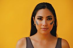 Serious Latina woman standing with mud mask on face, copy space