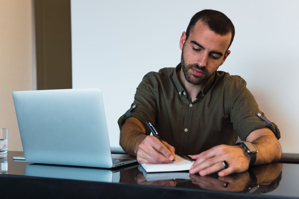 Man writing in notebook near laptop