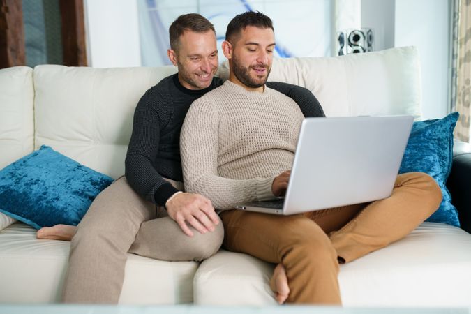 Two men cosy on sofa with laptop