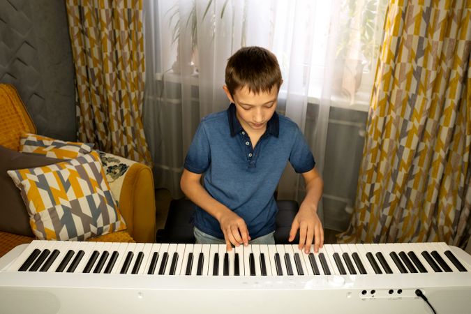 Boy playing digital piano in well-lit cozy living room.