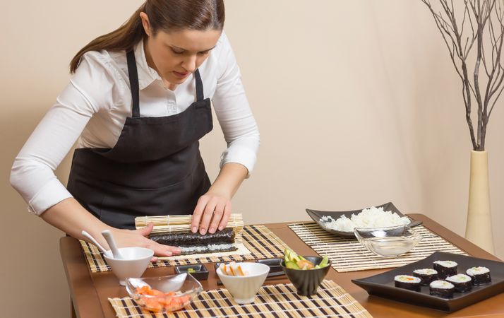 Portrait of female chef rolling sushi in nori sheet using mat