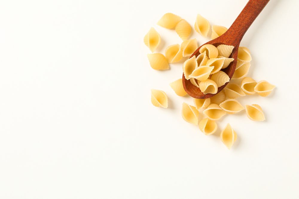 Wooden spoon with pasta on blank background, space for text. Dry uncooked whole pasta