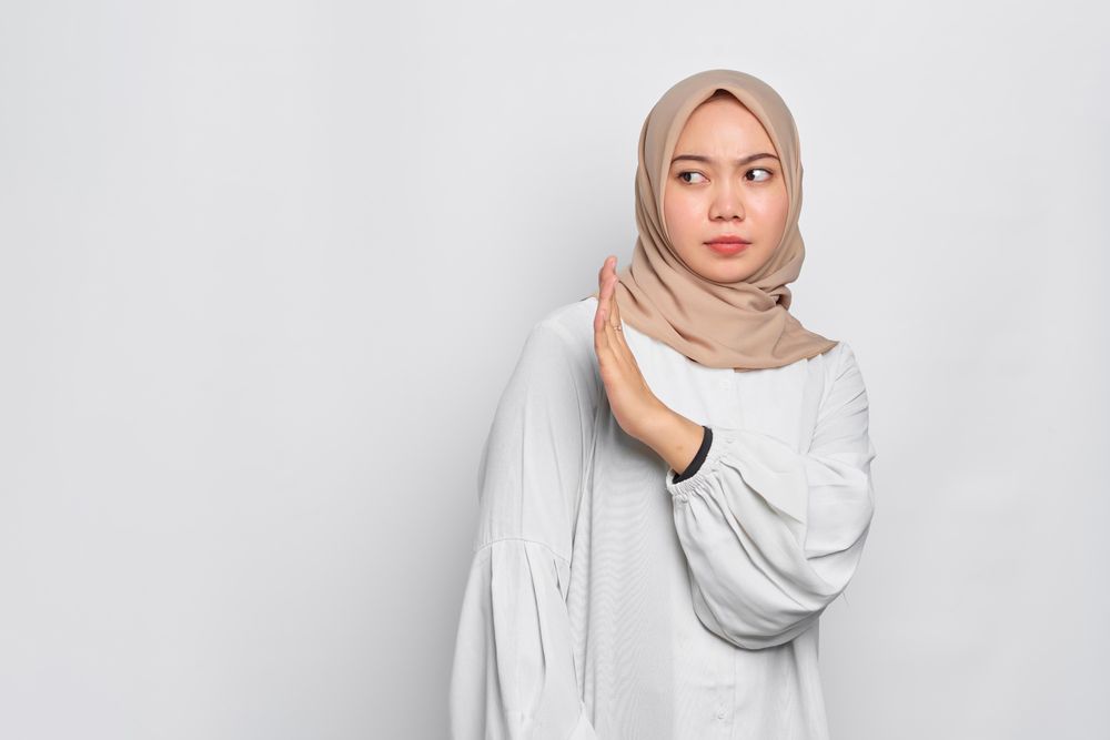 Serious Asian female in headscarf with hand up to the side