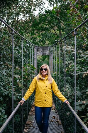 Cheerful female tourist standing on hanging bridge in summer