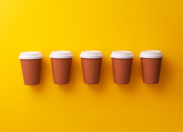 Single row of disposable coffee cups on yellow background