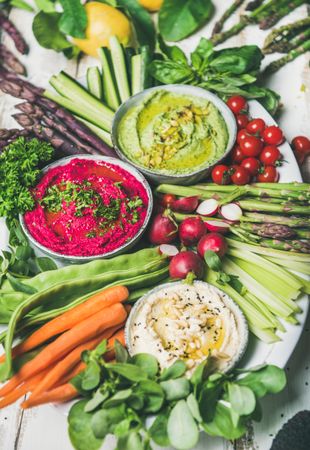 Top view of fresh colorful vegetables and dips with hummus, avocados, asparagus, carrots
