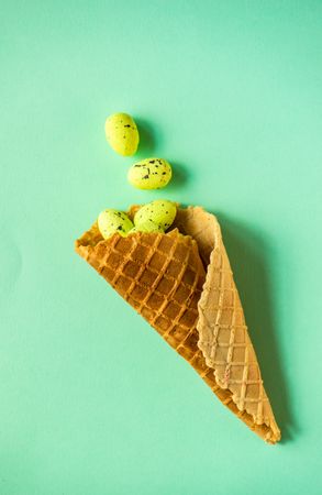 Waffle cone with green speckled eggs on green pastel background