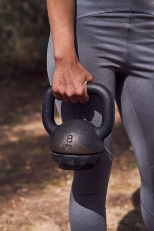 Crop sportswoman with kettlebell in nature