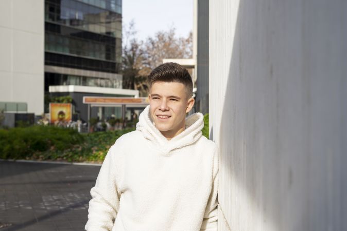 Portrait of smiling young male in bright hoodie leaning on wall outside