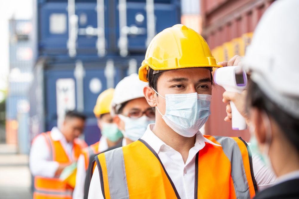 Line of workers on shipping dock having their temperature checked before a shift
