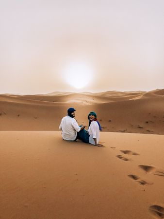 Man and woman sitting on sand dune in desert in Errachidia, Morocco