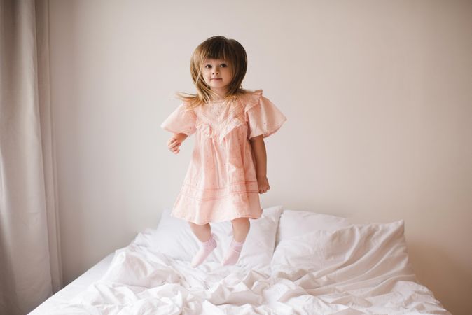 Girl in pink dress jumping on bed