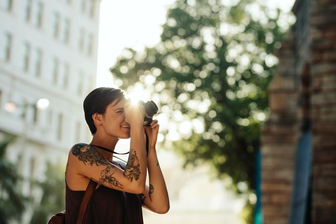 Woman traveler taking photo using her camera with sun in the background in the city