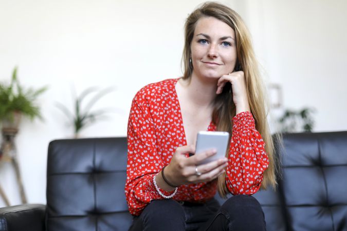 Blonde woman using a smartphone while sitting on leather sofa