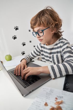 Boy in eyeglasses typing on laptop at home