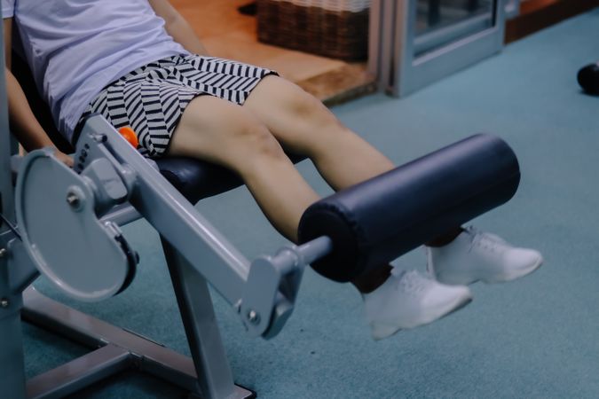 close up of woman's legs using leg extension device in indoor fitness center environment