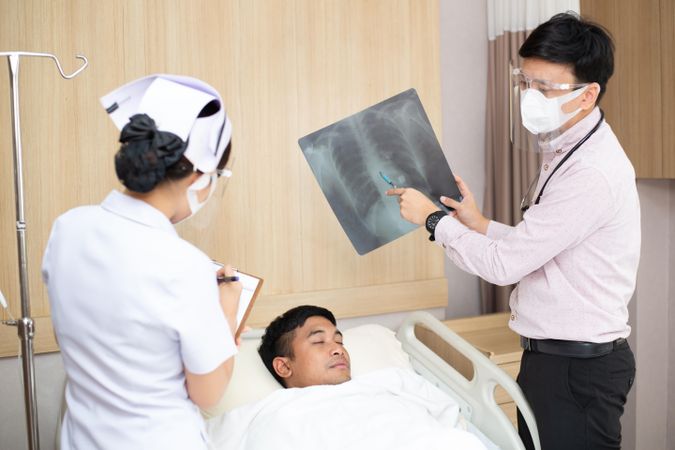 Patient lying in hospital bed with doctor and nurse showing chest X-ray