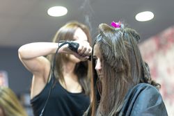 Long brunette haired woman having hair curled by stylist with ceramic hair iron