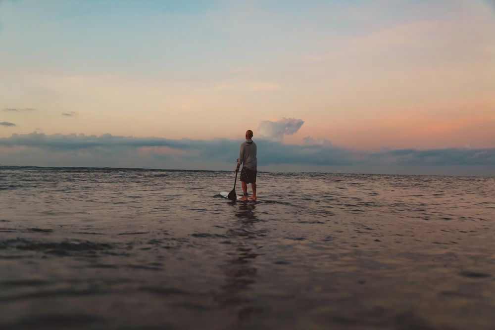 Man with paddle on surf board between waving water at sunset