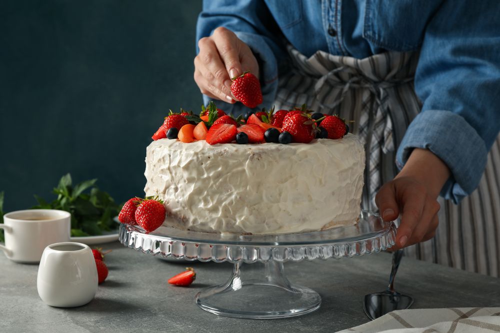 Woman puts strawberry on berry cream cake. Delicious dessert