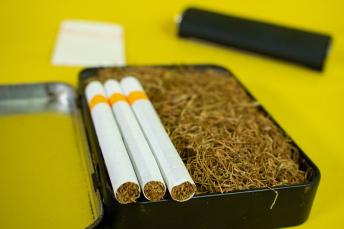 Close up of cigarettes resting on box of loose leaf tobacco