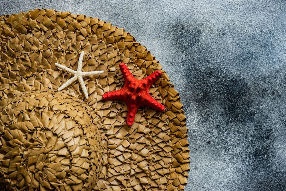 Top view of straw hat with seashells on grey counter