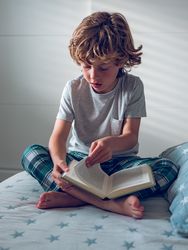 Little preschool boy sitting on bed and flipping through book