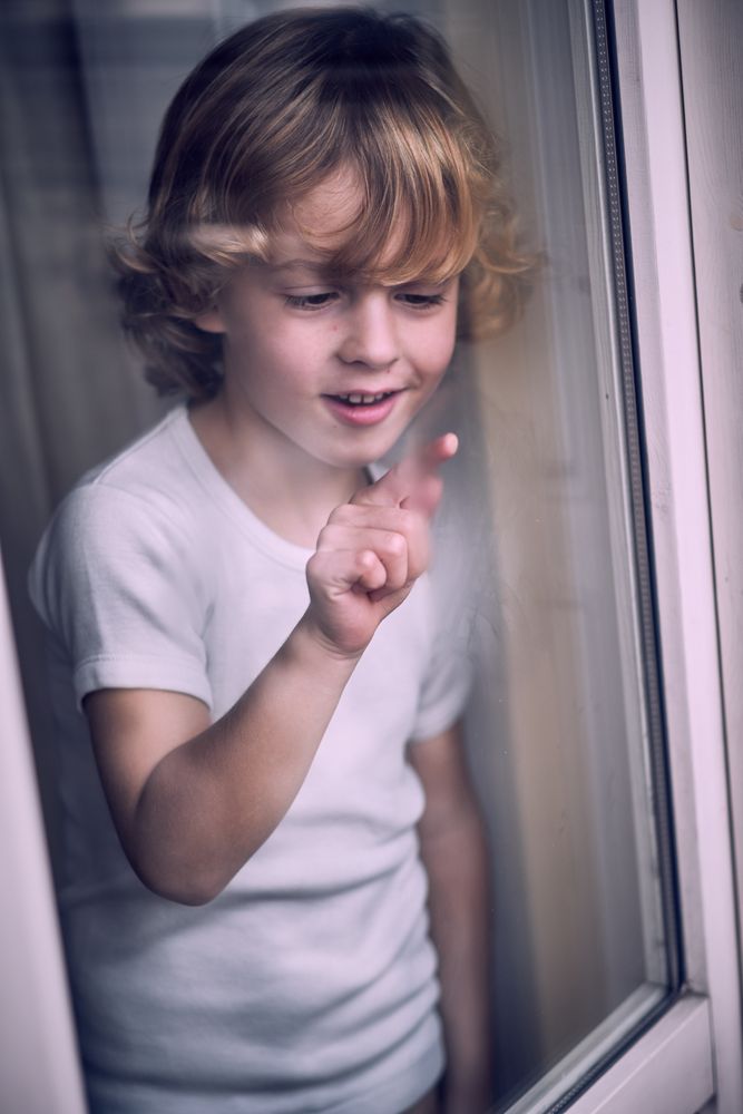 Happy little child drawing on misted window glass
