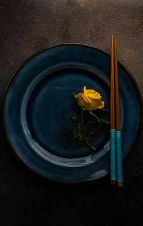 Blue table setting with single yellow rose and chopsticks
