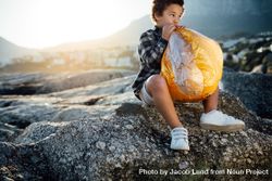Child sitting on a rock filling air into an inflatable ball 0PzEa4