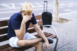Embarrassed man sitting on a bench in the street with his hands covering face
