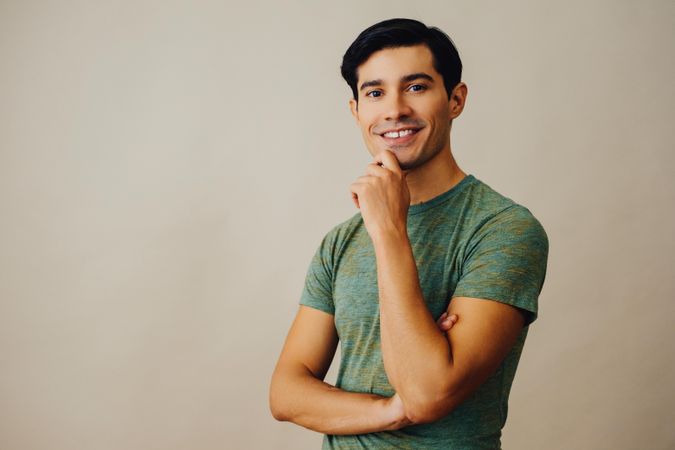 Happy Hispanic male holding his chin in neutral room, copy space