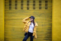 Trendy female standing near yellow wall on street