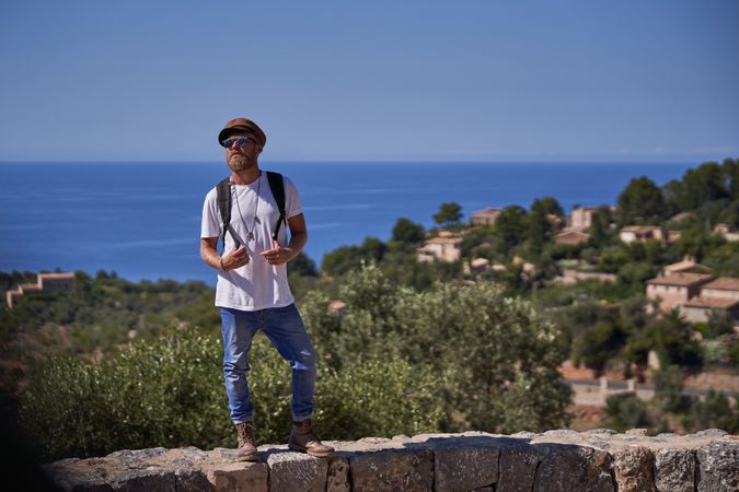 Unemotional male tourist in sunglasses standing on stony wall against sea