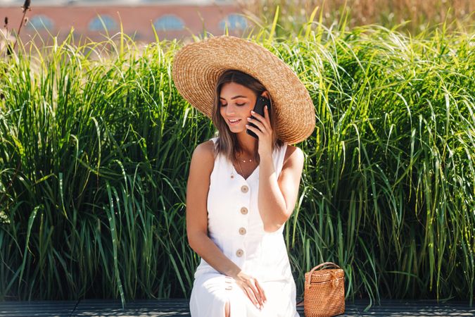 Woman sitting in front of long grass looking away while on phone