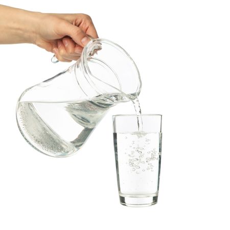 Hand pouring water in glass from pitcher in studio shoot