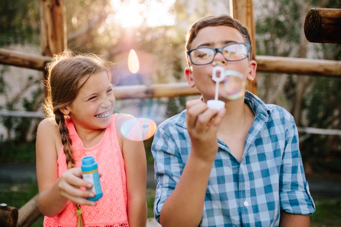 Boy blowing soap bubbles while an excited girl enjoys the bubbles