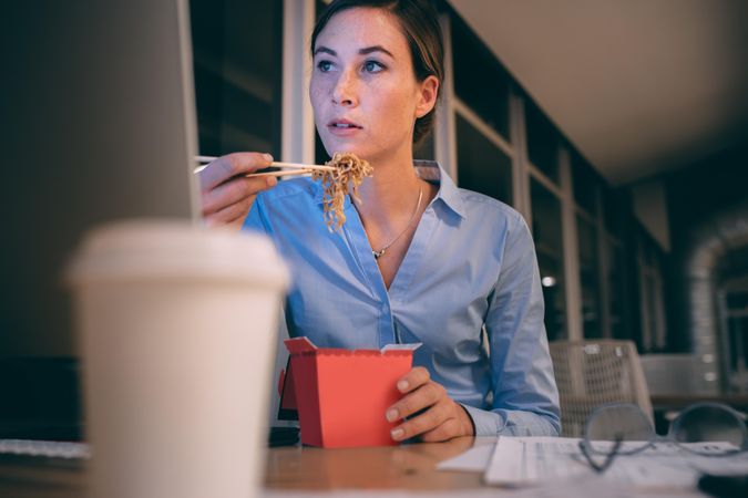 Businesswoman eating food sitting at her table while looking at the computer screen