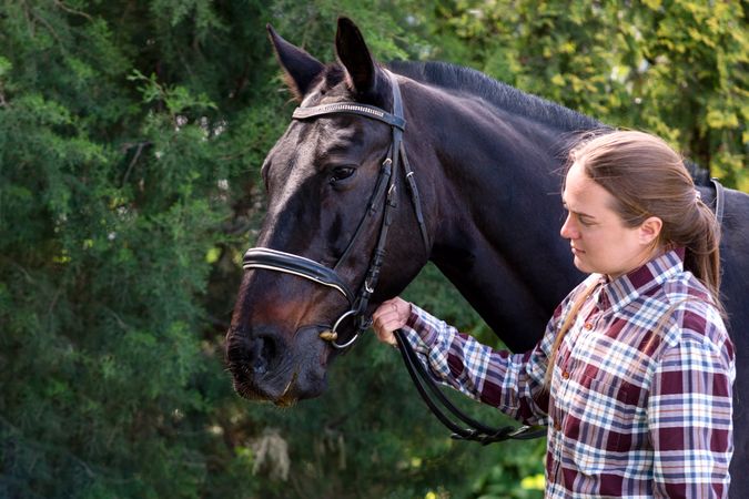 Woman holding a bridled horse outdoors.