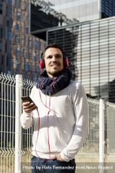 Young man listening to music on headphones while holding a mobile phone walking outdoor 0v3Goo