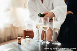 Woman in bathrobe pouring three glasses of sparkling wine 5k8N34