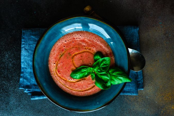 Top view of traditional Spanish gazpacho with basil leaf and olive oil garnish in blue bowl
