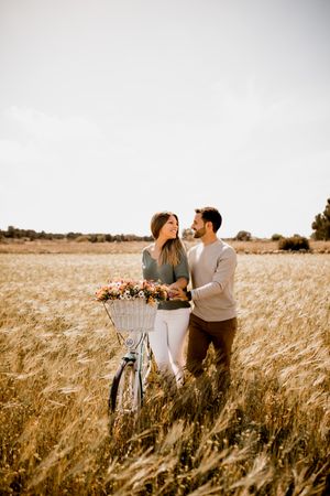 Sincere lovers posing by bicycle on rye field