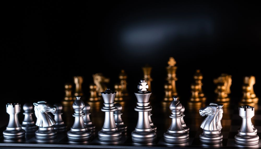 Silver and golden chess pieces on reflective board.