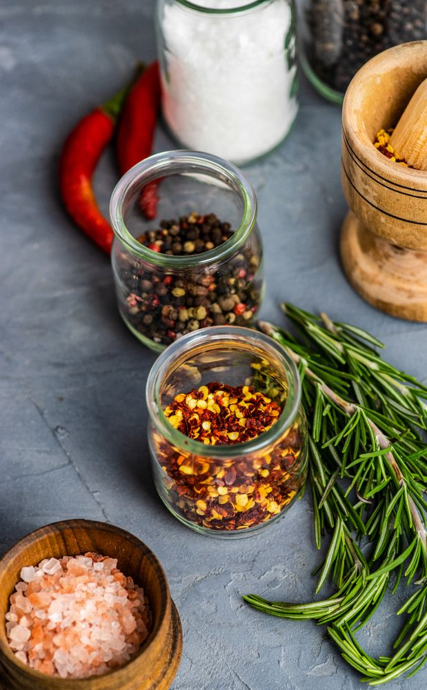 Two pots of chili flakes and peppercorns among herbs and seasoning