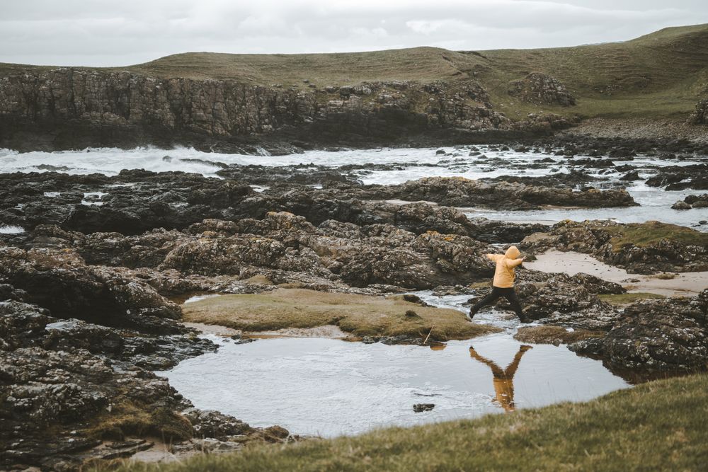 Man jumping over puddles of sea water on rocky shore