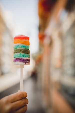 Hand holding delicious rainbow cake on city street