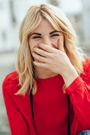 Shy blonde woman smiling with hand over her mouth