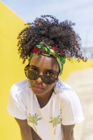 Serious Black woman looking up over sunglasses against yellow wall